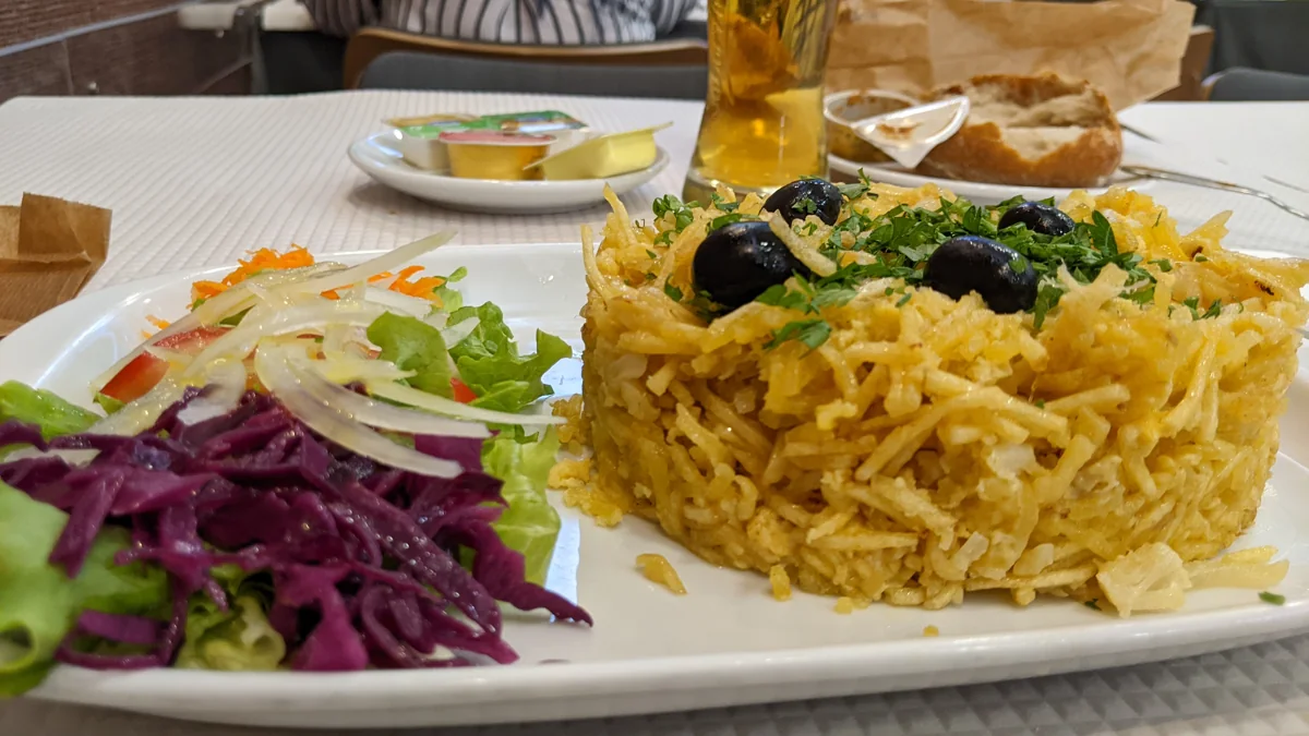 Bacalhau à Brás: Bacalao desmenuzado con papas paja, cebolla y huevo, terminado con aceitunas y perejil.