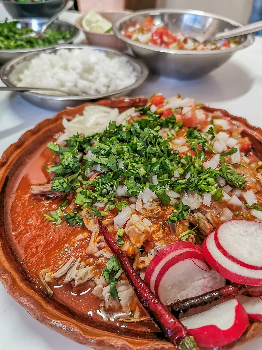 Birria de res: Guiso de carne en adobo de chiles, servido con consomé y tortillas.
