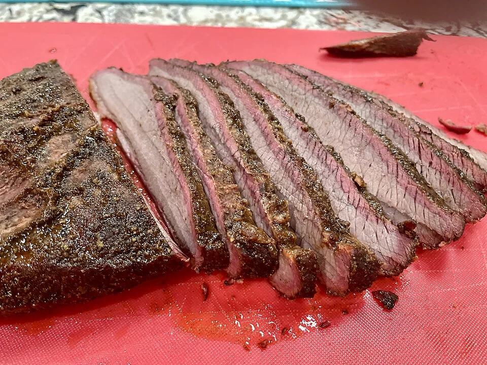 Brisket ahumado: Pecho de res ahumado lento con corteza de pimienta y sal.