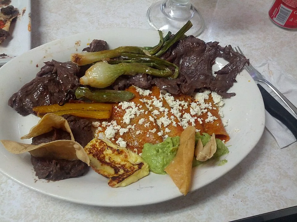Carne asada a la tampiqueña: Filete de res asado en tira acompañado de enchilada, rajas, frijoles y guacamole, creación de Tampico.