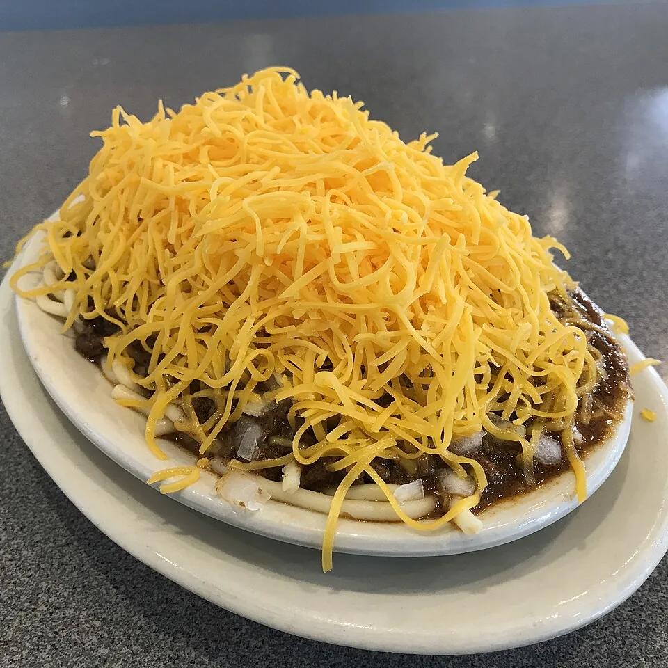 Chili de Cincinnati: Salsa de carne fina y especiada con toques de canela y chocolate, servida sobre espagueti y coronada con montaña de queso.
