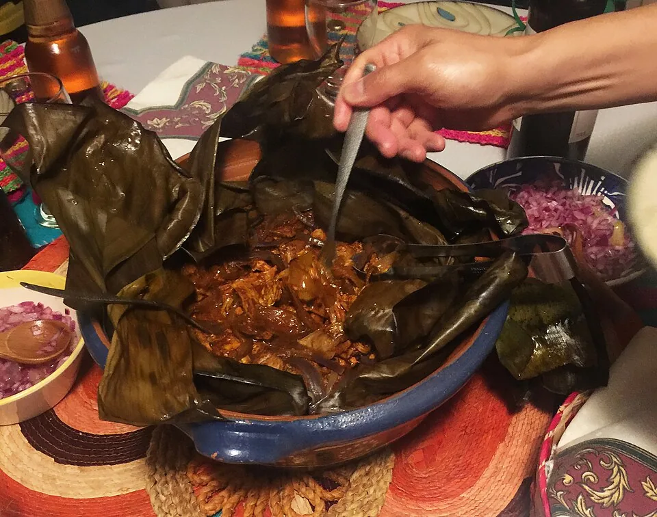 Cochinita pibil: Cerdo marinado en achiote y jugo de naranja agria, envuelto en hoja de plátano y cocido hasta deshebrarse.