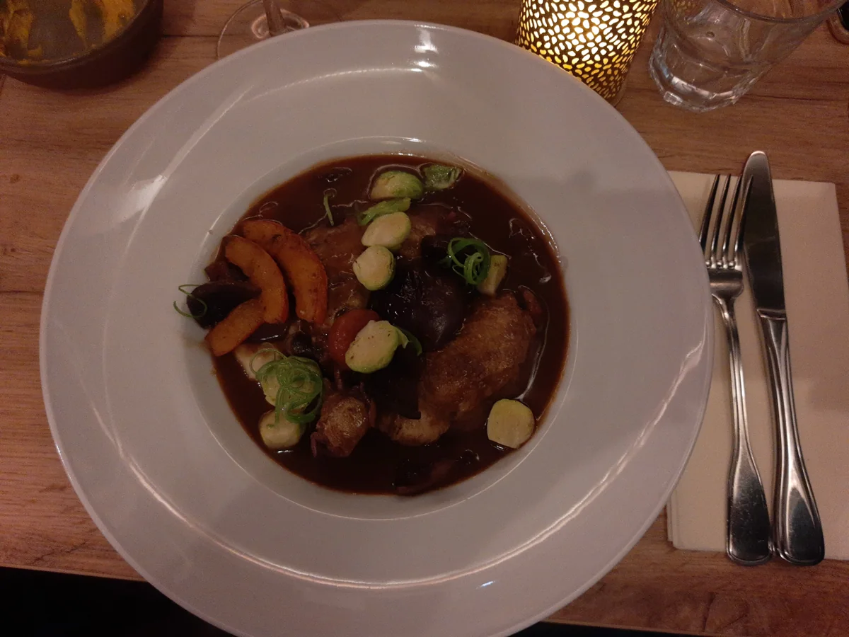 Coq au Vin: Pollo guisado en vino tinto con tocino, champiñones y cebollitas.