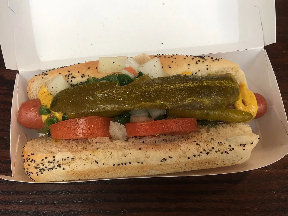 Hot dog estilo Chicago: Salchicha de res en pan con semillas de amapola y siete complementos clásicos, servida siempre sin cátsup.