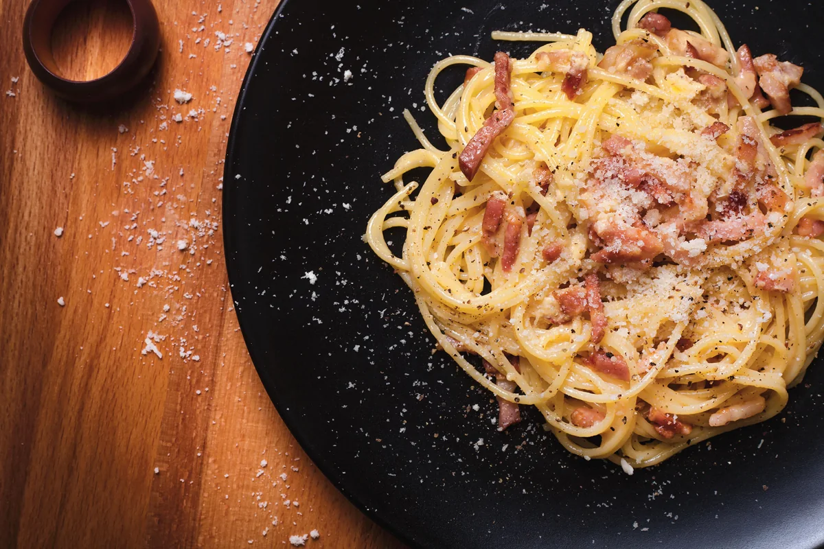 Pasta carbonara: Pasta romana con guanciale, pecorino, huevo y pimienta; cremosa por la emulsión y sin crema añadida.