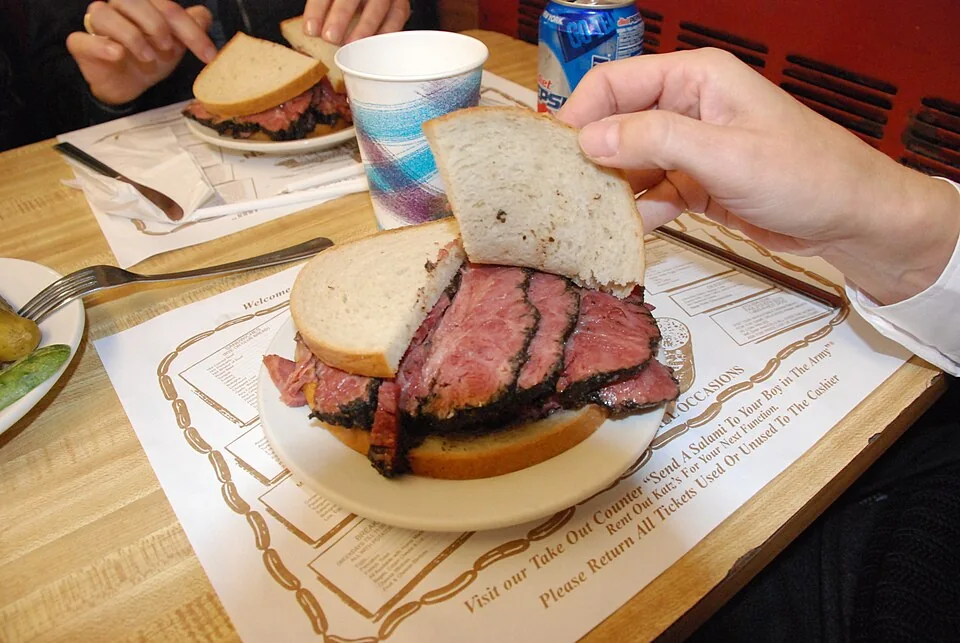 Pastrami on rye: Sándwich alto de pastrami de res curado y ahumado, cortado a mano, servido en pan de centeno con mostaza.