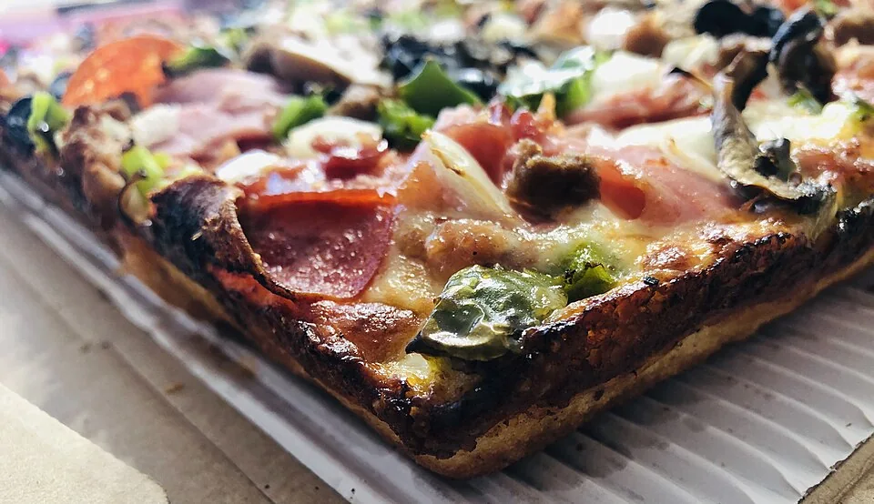 Pizza estilo Detroit: Pizza rectangular de masa esponjosa con orilla de queso caramelizado y franjas de salsa de tomate por encima.