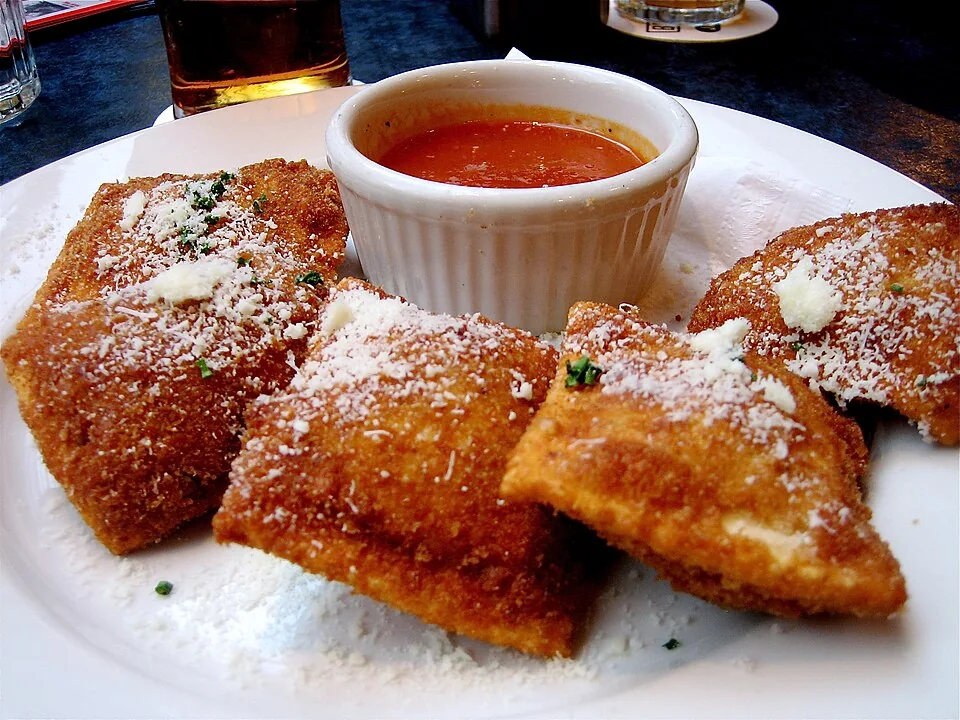 Ravioles fritos de San Luis: Ravioles empanizados y fritos hasta quedar dorados, servidos con queso parmesano y salsa marinara para mojar.