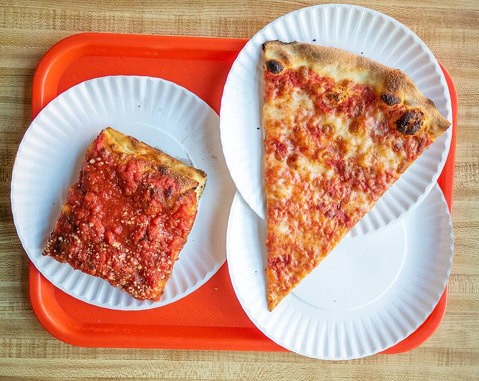 Rebanada de pizza estilo Nueva York: Rebanada grande, fina y flexible de masa crujiente, salsa de tomate y mozzarella, que se dobla para comer de pie.