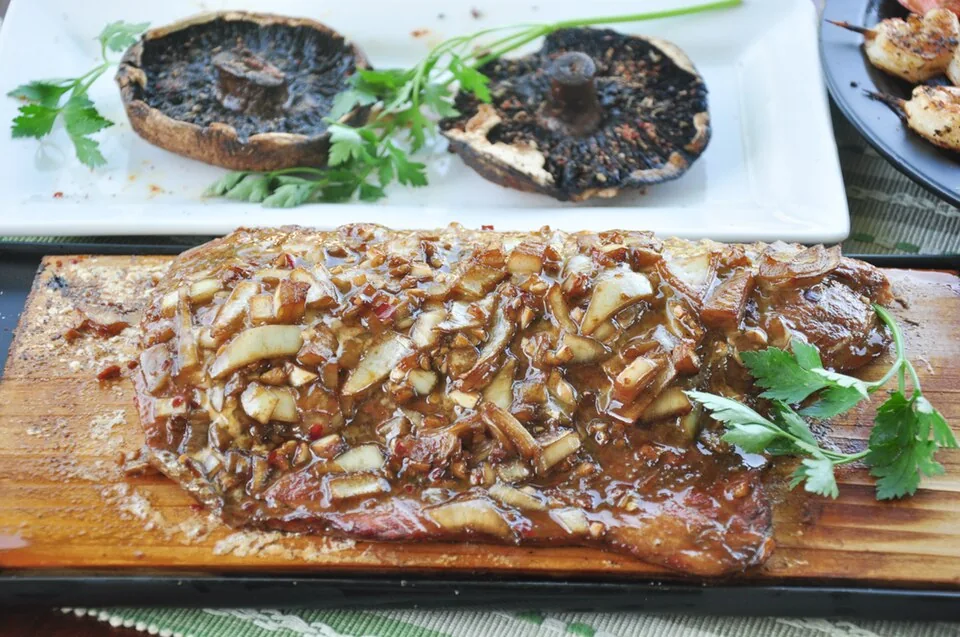Salmón a la tabla de cedro: Filete de salmón del Pacífico asado sobre una tabla de cedro que le aporta un característico aroma ahumado, tradición del noroeste.