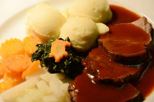 Sauerbraten: Asado alemán de res marinado en vino y vinagre, guisado lentamente y servido con salsa especiada.