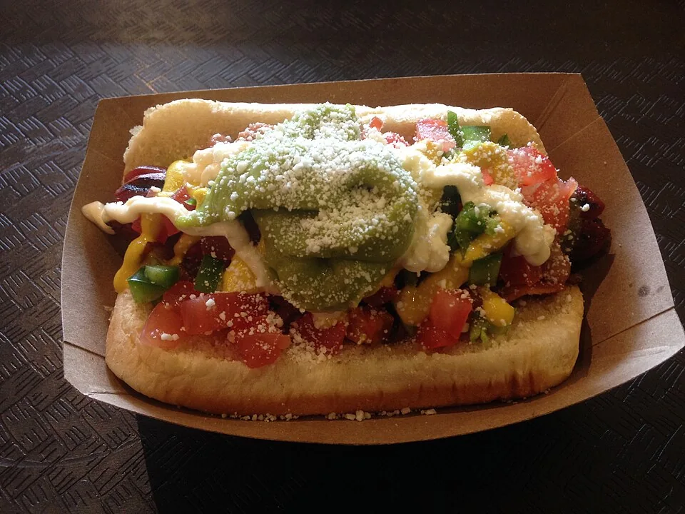 Sonoran hot dog: Hot dog envuelto en tocino a la plancha, servido en pan bolillo con frijoles pintos, tomate, cebolla, jalapeño y salsas.