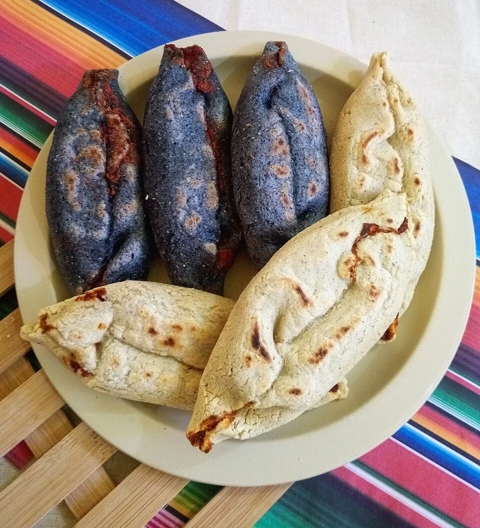 Tlayoyos: Gorditas ovaladas de masa de maíz rellenas de alverjón o frijol, cocidas en comal y cubiertas con salsa, queso y cebolla.