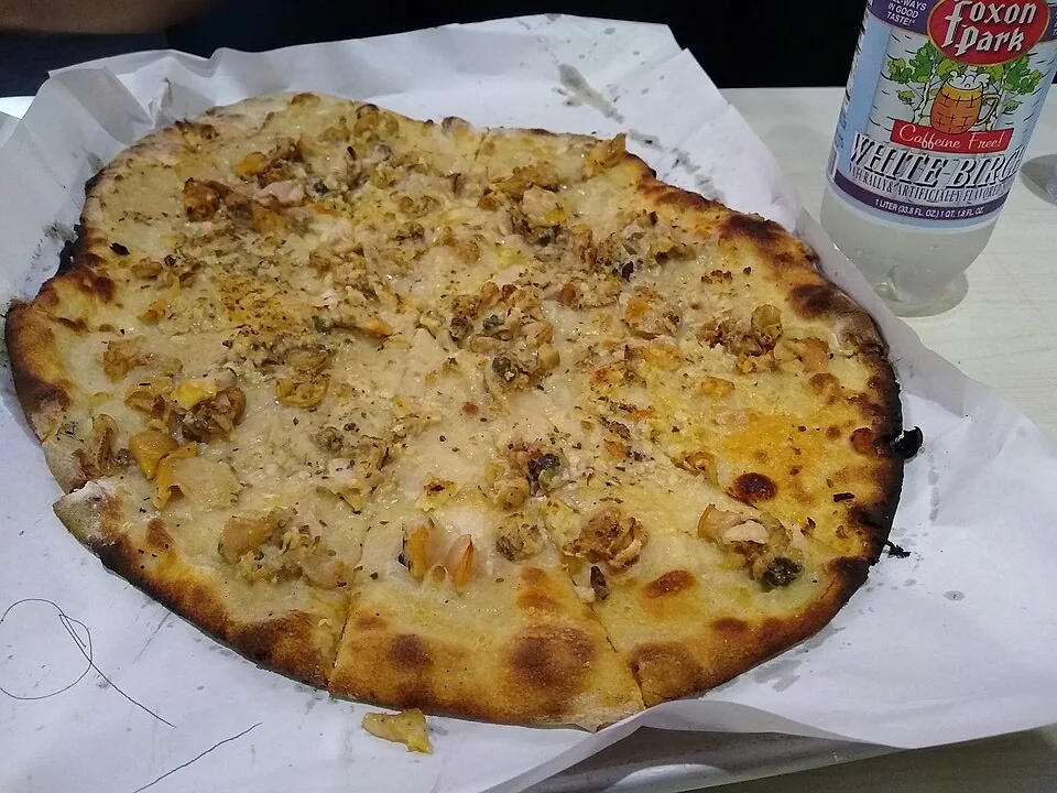 White clam apizza de New Haven: Pizza sin salsa de tomate, de corteza fina y carbonizada, cubierta de almejas frescas, ajo, orégano, aceite y queso rallado.
